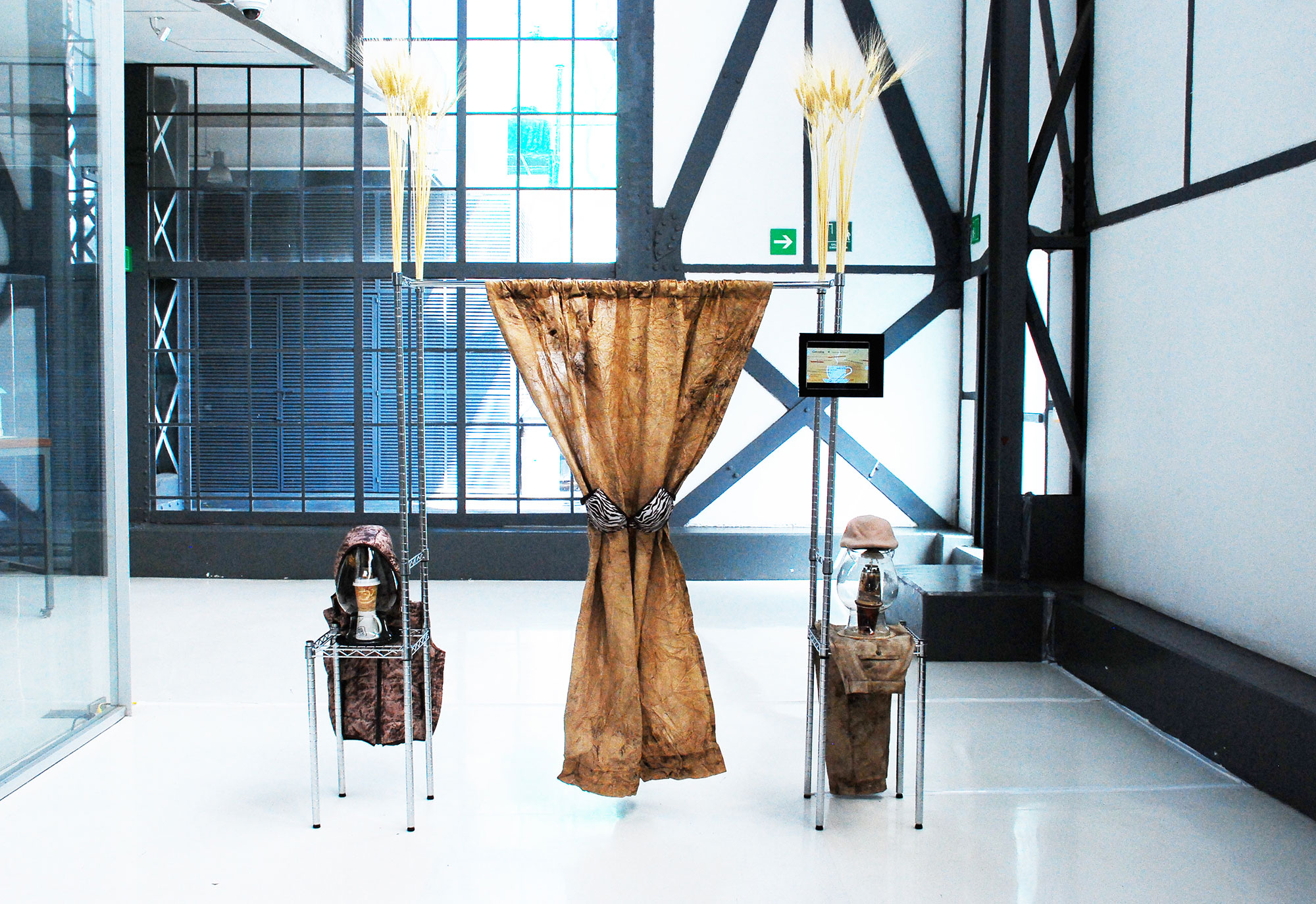 Debora Delmar Corp., Nectar of the Gods (from the series Body Blend Trade Culture), Chromed aluminum shelving units, coffee-stained curtain, bra, wheat, ipad, video, glass vases, ceramic coffee mugs, paper coffee cups, artificial hair, hooded puffy vest, coffee-stained khakis, cap, miniature table set with umbrella, miniature cabinet, 250 x 200 x 50 cm, Courtesy of the artist and Museo Universitareo del Chopo.
